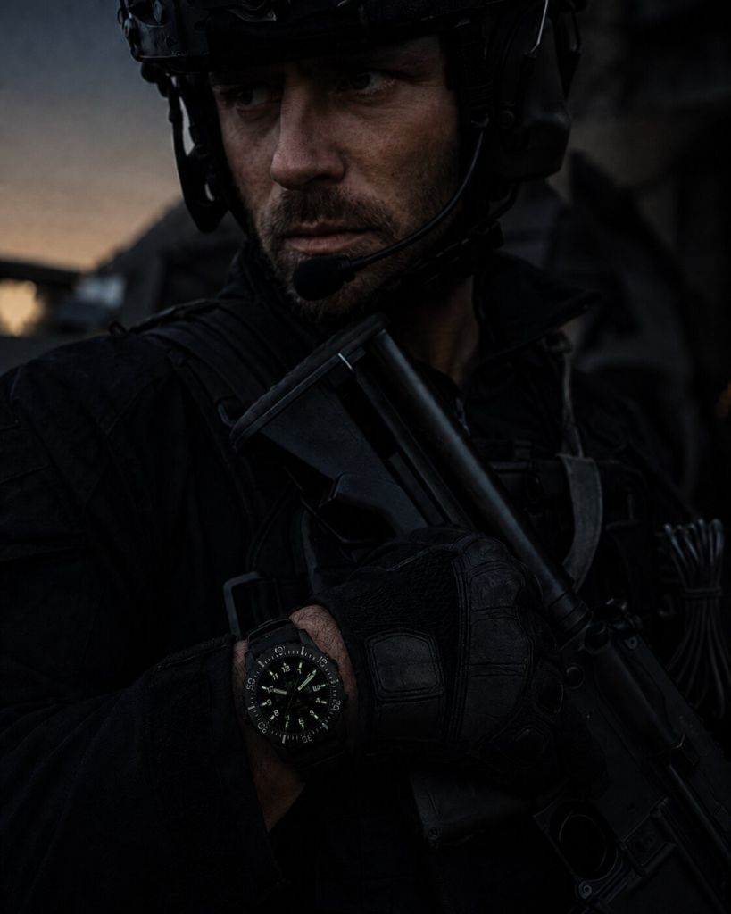 Military personnel wearing a black tactical tritium watch with glowing green markers in low-light conditions.